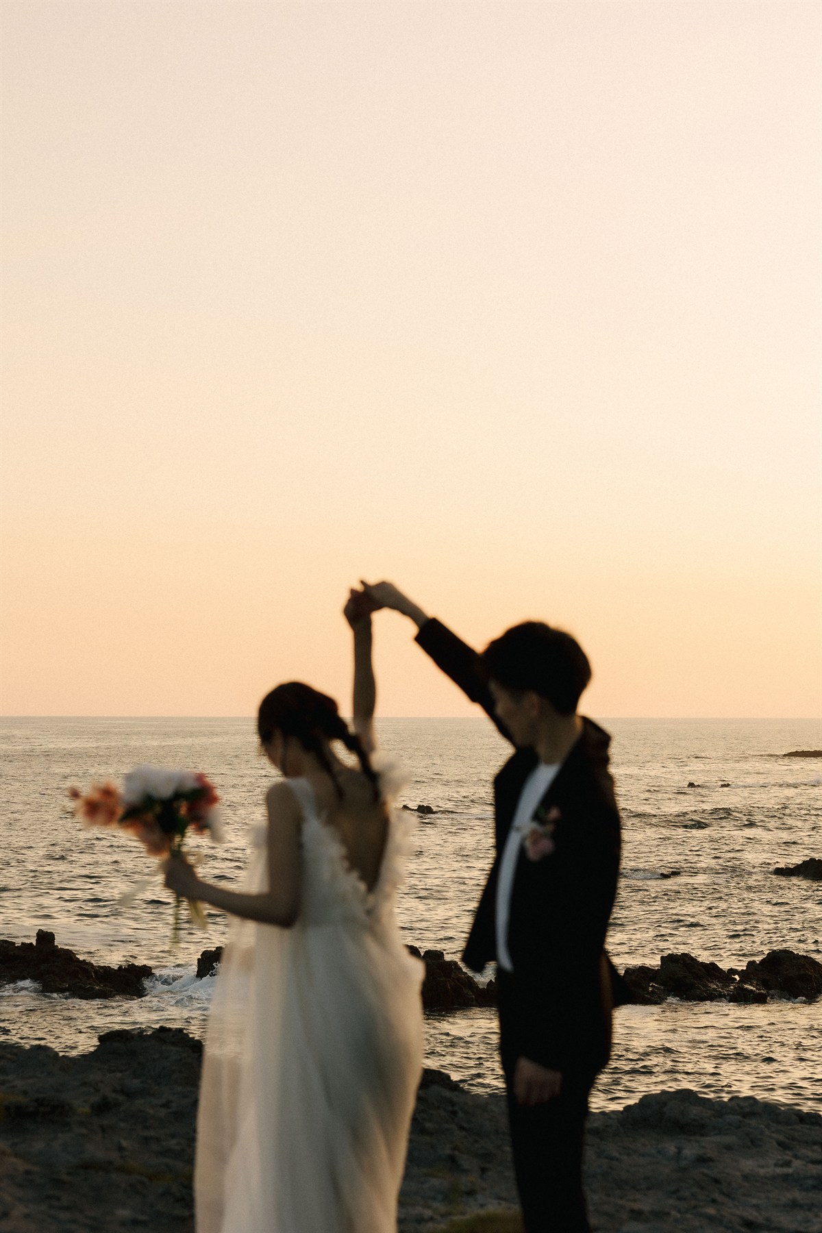 夕暮れの海辺で手を取り合う新郎新婦
