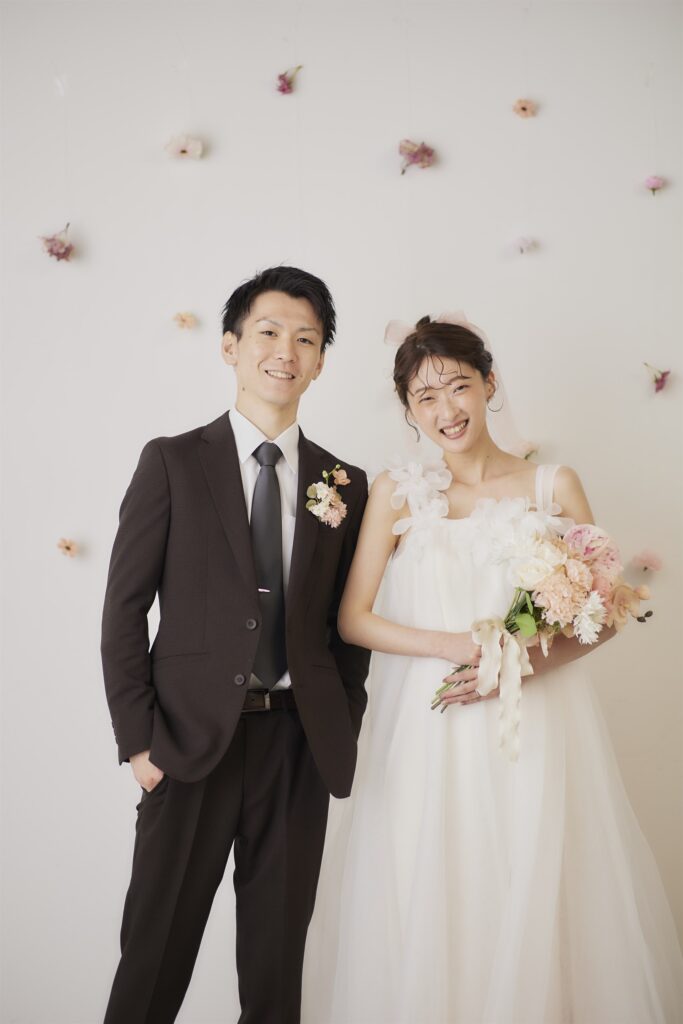 花をあしらった壁の前で笑顔の新郎新婦