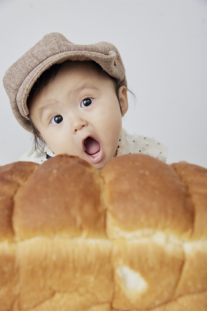 食パンを抱えて口を開ける赤ちゃんのベビーフォト